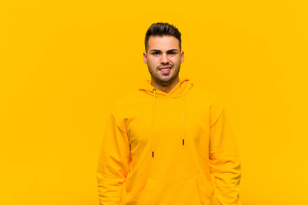 young hispanic man looking puzzled and confused, biting lip with a nervous gesture, not knowing the answer to the problem against orange wall - Fotoğraf, Görsel