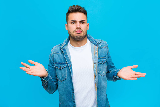young hispanic man looking puzzled, confused and stressed, wondering between different options, feeling uncertain against blue background - Photo, Image