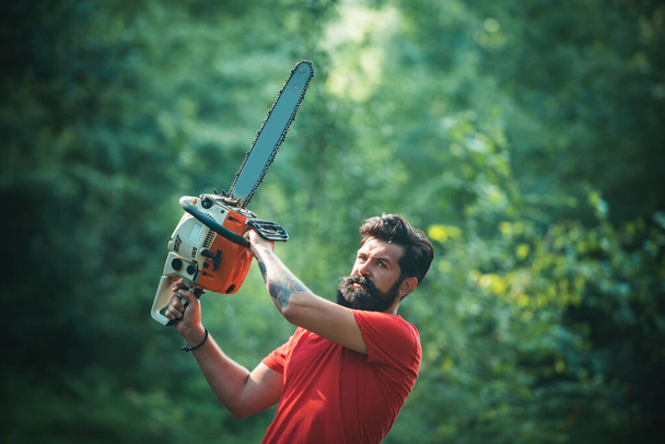 Woodworkers lumberjack. Lumberjack on serious face carries chainsaw. Man doing mans job. Lumberjack worker walking in the forest with chainsaw. - Photo, Image