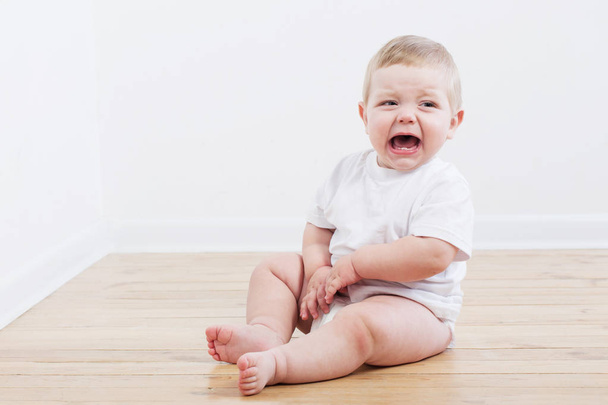 baby crying sitting on wooden floor - Zdjęcie, obraz