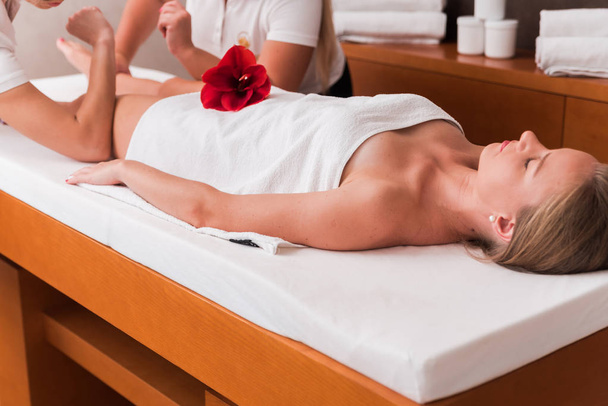 woman getting anti cellulite massage of legs in spa salon. Flower decoration. Two masseurs near making royal foot massage - Photo, image