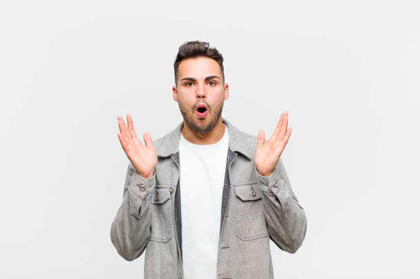 young hispanic man looking shocked and astonished, with jaw dropped in surprise when realizing something unbelievable against gray background - Fotoğraf, Görsel