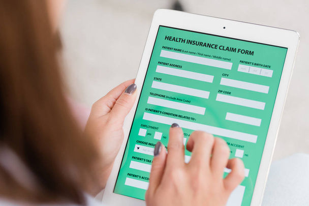 Hände einer jungen Frau mit Touchpad und Krankenversicherungsformular beim Ausfüllen persönlicher Daten - Foto, Bild