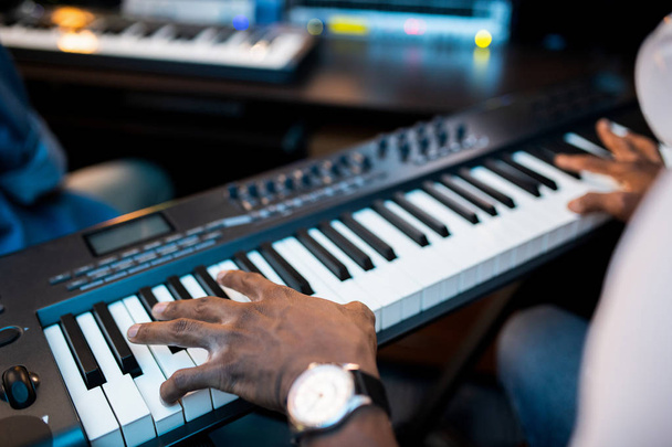 Hands of young African composers or musician touching keys of pianoboard while working in sound recording studio - Photo, Image