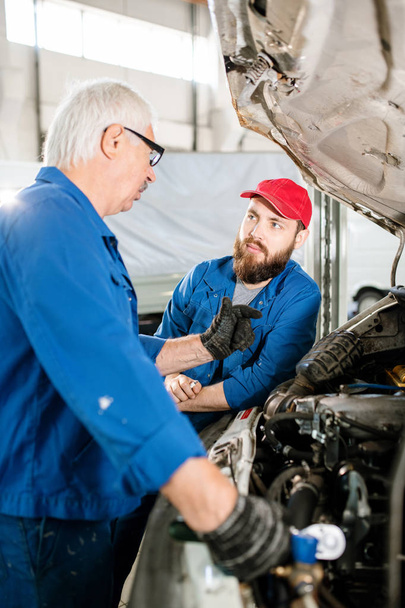 Зрелый опытный работник технической службы ремонта объяснил молодому коллеге, как обслуживать автомобили
 - Фото, изображение