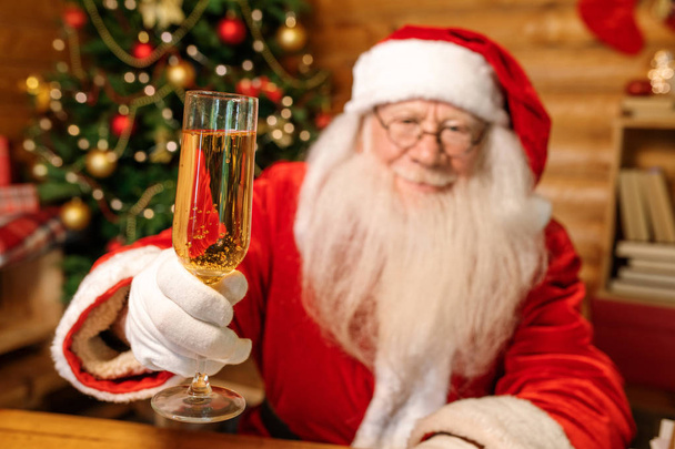 Happy Santa Claus cheering with flute of champagne in front of camera while wishing you merry Christmas - Foto, afbeelding