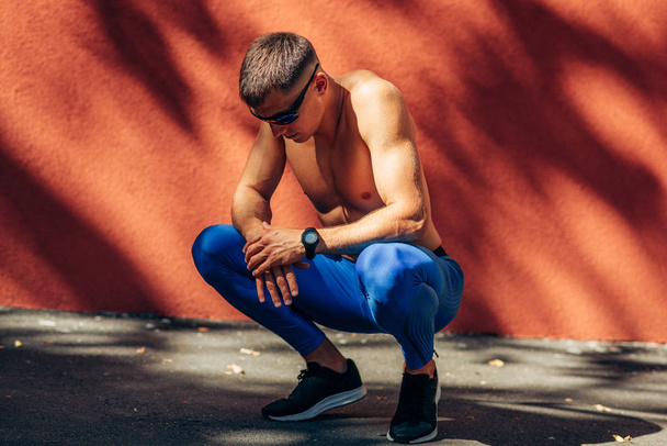 Jovem atleta homem descansando contra parede de concreto laranja ao ar livre. Desportista sem camisa profissional descansando após sessão de treinamento. Pessoas, esporte e estilo de vida saudável
 - Foto, Imagem