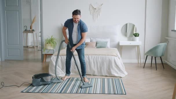 Cheerful man using vacuum cleaner during clean-up at home dancing having fun - Séquence, vidéo