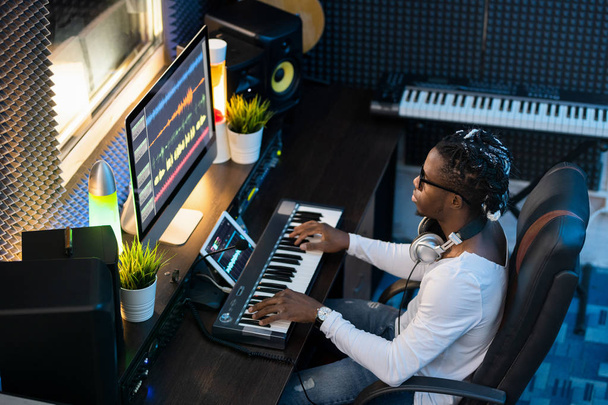 Joven músico de etnia africana sentado en el estudio de grabación, haciendo nueva música y mezclando sonidos en la computadora
 - Foto, Imagen