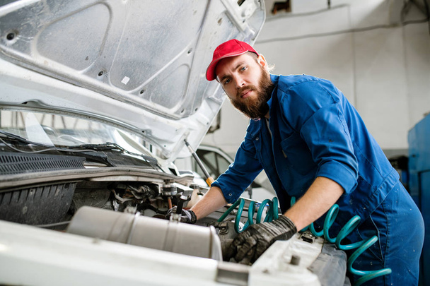 Серйозний технік в робочому одязі дивиться на вас під час ремонту двигуна зламаної машини в його майстерні або ангарі
 - Фото, зображення
