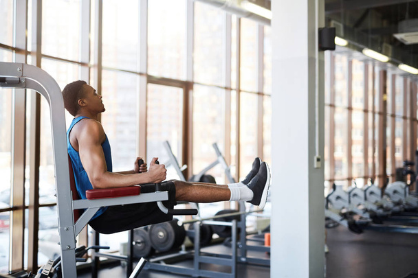 Retrato de vista lateral del hombre afroamericano muscular usando máquinas de ejercicio durante el entrenamiento en el gimnasio moderno contra la ventana, espacio para copiar
 - Foto, imagen
