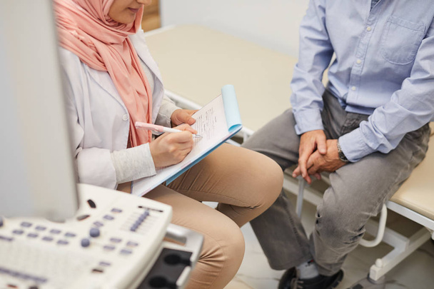 Одяг арабських жінок-лікарів, що пишуть на дошці для кліпів, під час обстеження старшого пацієнта в медичній клініці, копіюйте місце. - Фото, зображення