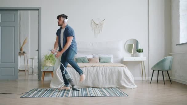 Cheerful guy vacuuming carpet at home and dancing with vacuum cleaner - Filmati, video