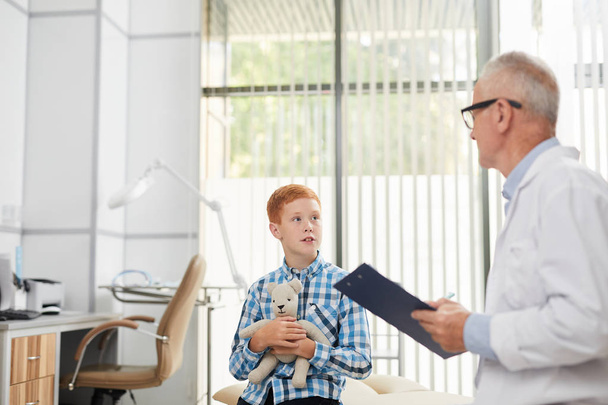 Porträt des niedlichen rothaarigen Jungen im Gespräch mit dem Oberarzt während der Konsultation in der Kinderklinik, Kopierraum - Foto, Bild