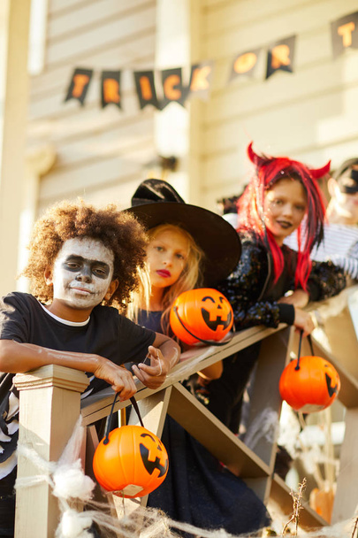 Groupe multi-ethnique d'enfants portant des costumes d'Halloween regardant la caméra tout en se tenant debout sur les escaliers de la maison décorée dans la saison des bonbons ou des bonbons
 - Photo, image