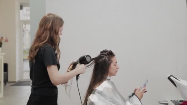 Dívka kadeřník suší vlasy na klienta s fénem na kadeřnictví. - Záběry, video