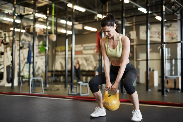 Portrait complet de femme forte soulevant kettlebell pendant l'entraînement croisé dans la salle de gym moderne, espace de copie
 - Photo, image