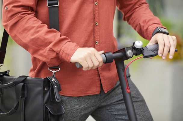 Closeup of contemporary young man riding electric scooter in city street, focus on male hands holding handlebars, copy space - Foto, Bild