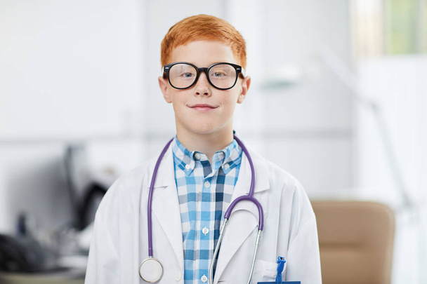 Vyötärö ylös muotokuva söpö punainen tukkainen poika poseeraa lääkäri yllään valkoinen takki ja hymyillen onnellisesti kameralle, kopioi tilaa
 - Valokuva, kuva