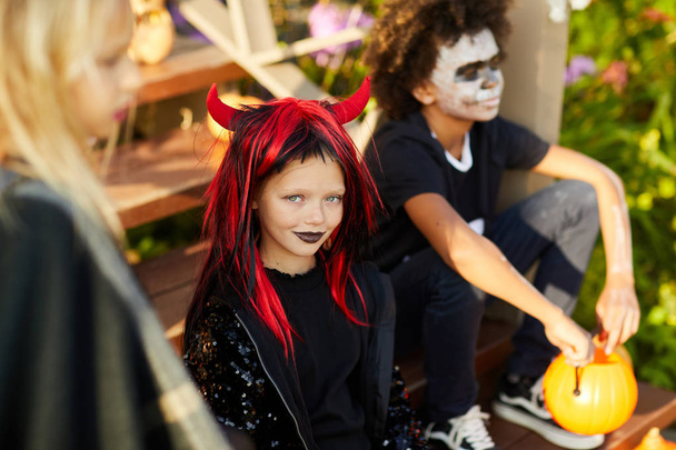 Hoge hoek portret van kinderen truc of traktatie op Halloween, glimlachend meisje kijken naar de camera terwijl zitten op de trap van versierd huis - Foto, afbeelding