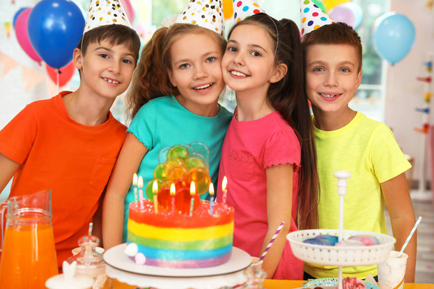 Niños felices cerca de la torta con velas en la fiesta de cumpleaños en interiores
 - Foto, Imagen