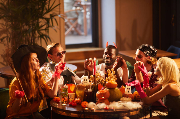 Grupo de amigos vestindo trajes de Halloween realizando ritual mágico sentado mesa redonda na festa, espaço de cópia
 - Foto, Imagem
