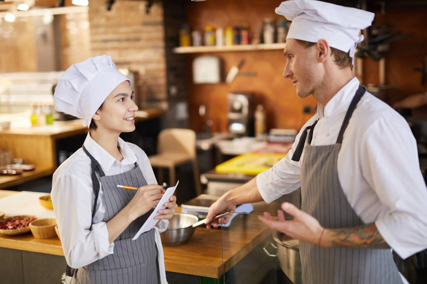 Vista laterale ritratto di chef professionista formazione giovane cuoco prendere appunti mentre si lavora in cucina ristorante
 - Foto, immagini