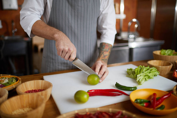 Close up de irreconhecível chef de corte de limas e pimenta enquanto cozinha comida asiática picante na cozinha do restaurante, espaço de cópia
 - Foto, Imagem