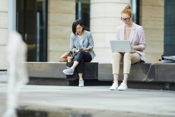 Retrato de larga duración de dos jóvenes empresarias que usan computadoras portátiles mientras trabajan al aire libre en un entorno urbano, espacio para copiar
 - Foto, imagen