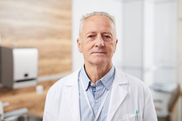 Taillenhoch Porträt des leitenden Arztes, der gelassen in die Kamera lächelt, während er im Büro einer modernen Klinik posiert, Kopierraum - Foto, Bild