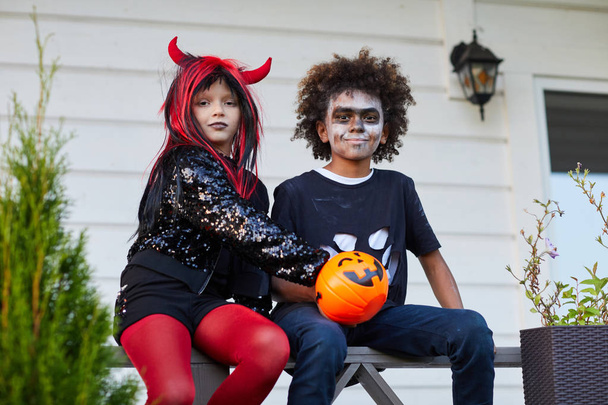 Porträt zweier glücklicher Kinder, die nach einem Trick im Freien Halloween-Bonbons essen oder sich gemeinsam behandeln - Foto, Bild