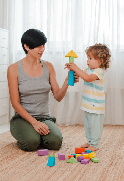 Mutter und Kind spielen auf dem Fußboden im Kinderzimmer. Mutter und kleiner Junge bauen einen Turm aus farbigen Blöcken. - Foto, Bild