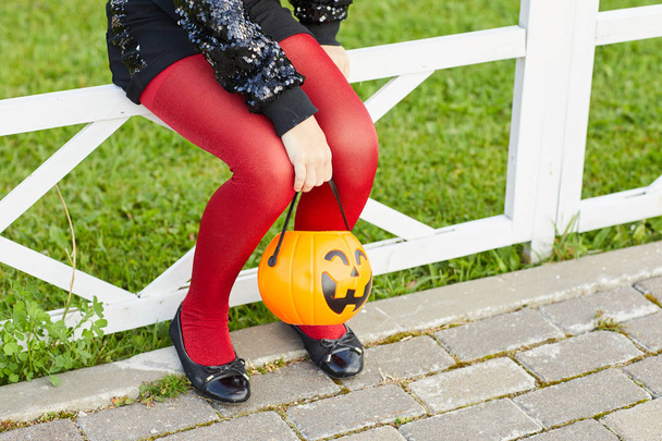 Low section portrait of unrecognizable girl holding pumpkin basket while trick or treating on Halloween, copy space - Photo, Image