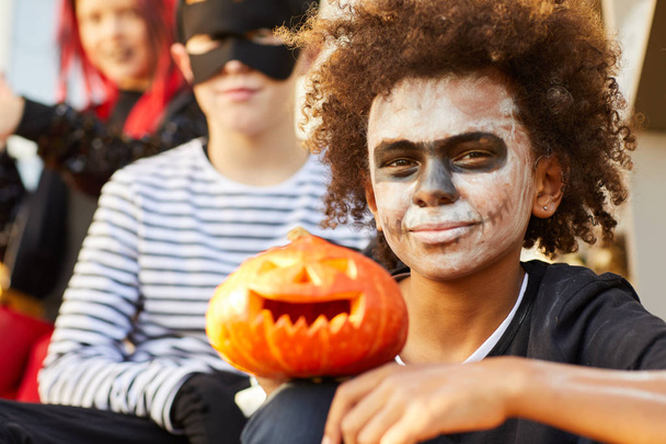 Retrato de menino afro-americano vestindo traje de Halloween olhando para a câmera enquanto sentado ao ar livre com amigos, espaço de cópia
 - Foto, Imagem