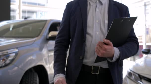 salon samochodowy, kierownik samochodu mężczyzna trzyma w rękach klucze do nowego samochodu na sprzedaż w salonie - Materiał filmowy, wideo
