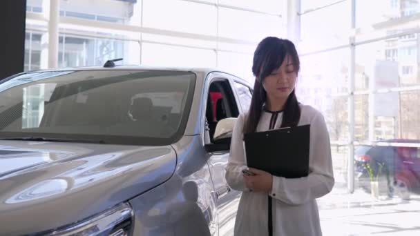 πορτρέτο του χαμογελαστού διαχειριστή θηλυκό δίνοντας θετική χειρονομία αντίχειρες κοντά στο νέο αυτοκίνητο στο κέντρο auto - Πλάνα, βίντεο