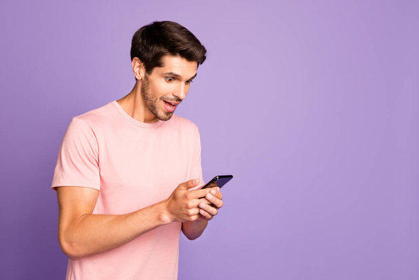 Profile side view portrait of his he nice attractive cheerful glad focused guy wearing pink tshirt holding in hands using digital device gadget isolated on violet purple lilac pastel color background - Photo, Image