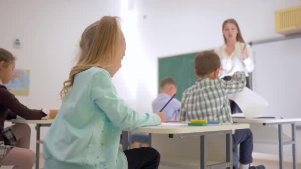 Porträt eines Schulkindes am Schreibtisch während des Unterrichts im Klassenzimmer der Grundschule auf unfokussiertem Hintergrund - Filmmaterial, Video