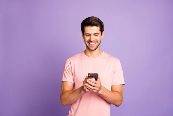 Πορτρέτο του ο συμπαθητικός ελκυστικός χαρούμενος χαρούμενος τύπος φορώντας ροζ μπλουζάκι κρατώντας στα χέρια χρησιμοποιώντας 5g app cell σύγχρονη τεχνολογία απομονωμένη πάνω βιολετί μωβ λιλά παστέλ χρώμα φόντο - Φωτογραφία, εικόνα