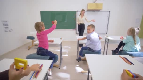 kinderen collegegeld, vrolijke opvoeder vrouw in de buurt van boord voert cognitieve les voor schattige leerlingen aan het bureau in de klas van School - Video