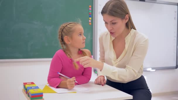 Schulvorbereitung: Lehrerin hilft Mädchen beim Lernen mit Plastikfiguren am Tisch neben der Tafel im Klassenzimmer - Filmmaterial, Video