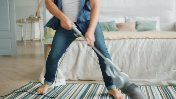 Tilt-up of joyful man vacuuming carpet in apartment pretending to play guitar - 映像、動画