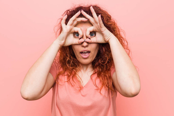 Молодая натуральная и подлинная рыжая женщина показывает знак одобрения над глазами
 - Фото, изображение