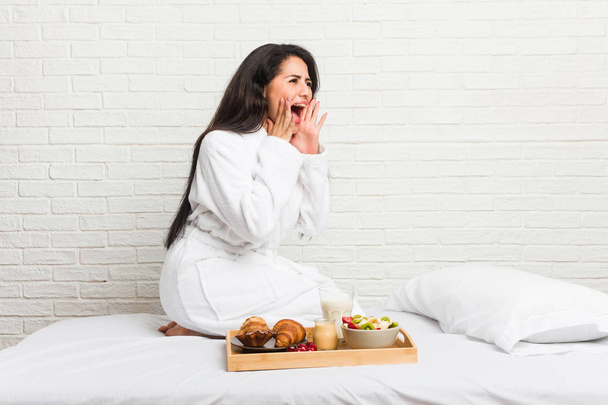 Joven mujer con curvas tomando un desayuno en la cama grita fuerte, mantiene los ojos abiertos y las manos tensas
. - Foto, Imagen