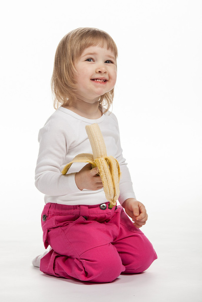 The smiling baby girl is eating ripe banana - Foto, imagen