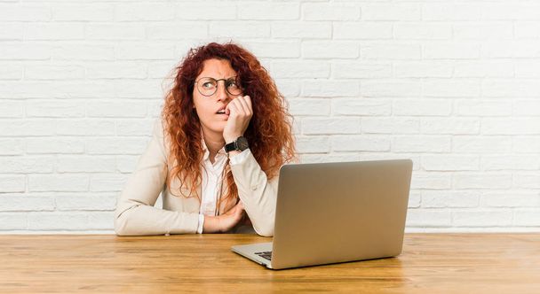 Nuori punapää kihara nainen työskentelee hänen kannettava tietokone puree kynnet, hermostunut ja hyvin ahdistunut
. - Valokuva, kuva