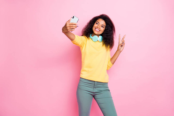 Portrait of positive cheerful photographer african girl influencer make v-signs take selfie use cellphone as camera have trip wear yellow stylish trendy pullover pants isolated pastel color background - Fotó, kép