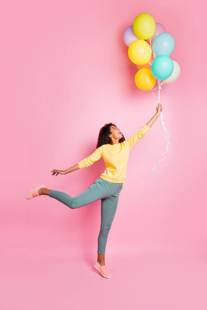 Weekend vacation freedom concept. Vertical full length photo of cute romantic lovely dreamy nice positive hipster in yellow jumper holding baloons want to fly up isolated pastel color background - Фото, изображение