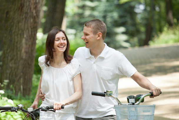 Happy νεαρό ζευγάρι περπάτημα σε ένα πάρκο με ποδήλατα - Φωτογραφία, εικόνα
