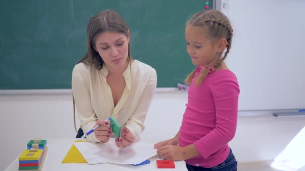 Çocuk eğitimi, genç bir öğretmen okul masasının yanındaki masada plastik figürler kullanarak akıllı kız öğrencilere ders veriyor. - Video, Çekim